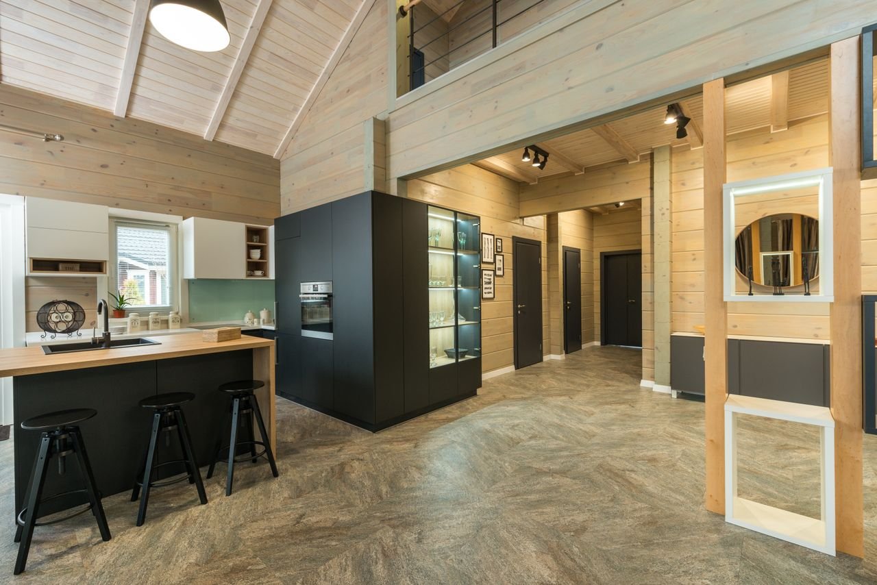 Corridor of spacious cottage with wooden walls leading to counter with bar chairs in kitchen equipped with built in appliances