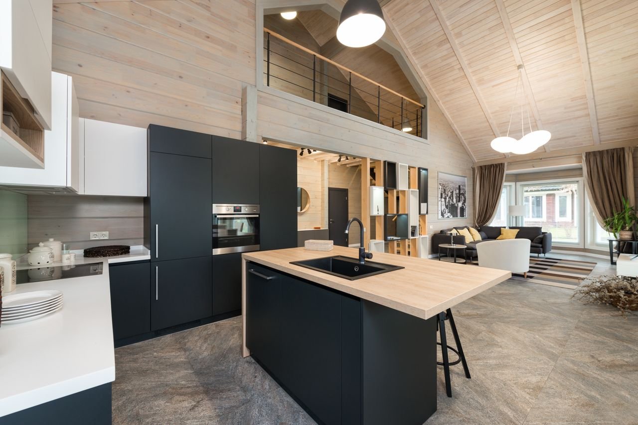 Stylish matte furniture and built in appliances under glowing lamp hanging on wooden ceiling with living zone in spacious house