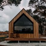 Home A contemporary wooden cabin in a rural outdoor setting surrounded by tall trees.